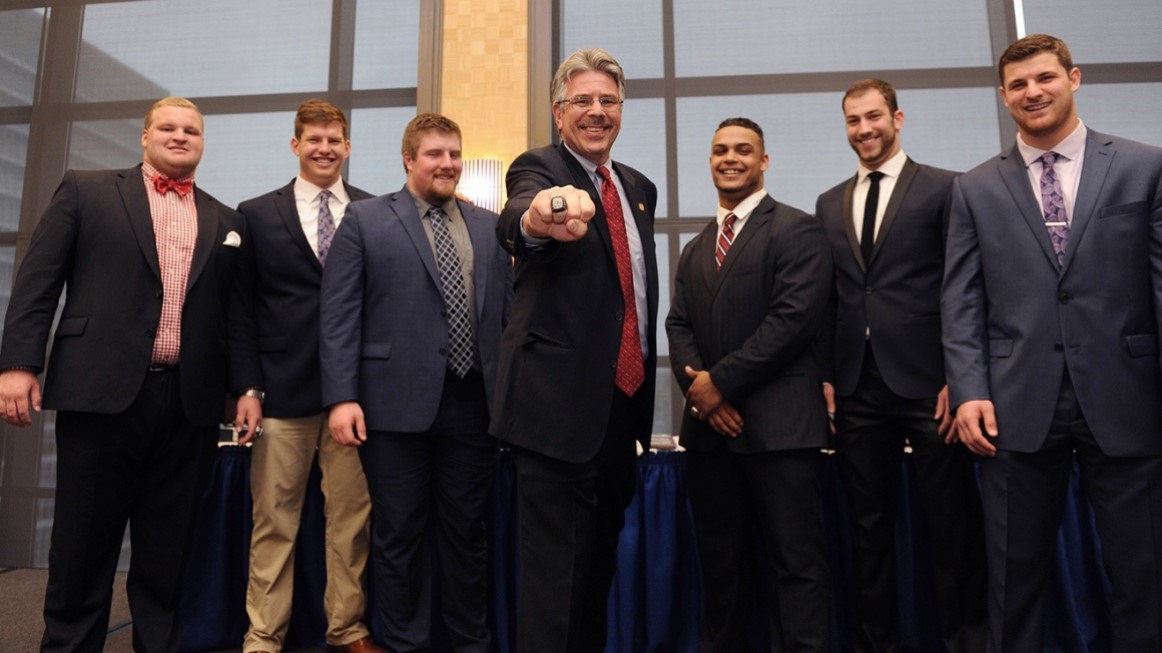 President Gormley holding out Duquesne ring with student football players