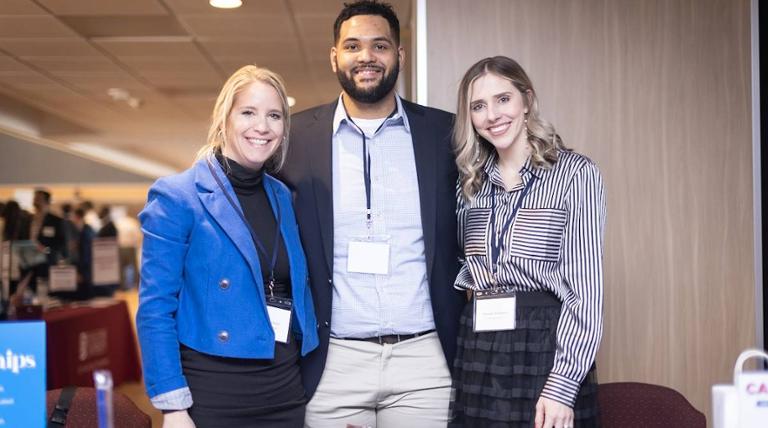 three recruiters smiling and posing in front of their table at the biannual career fair