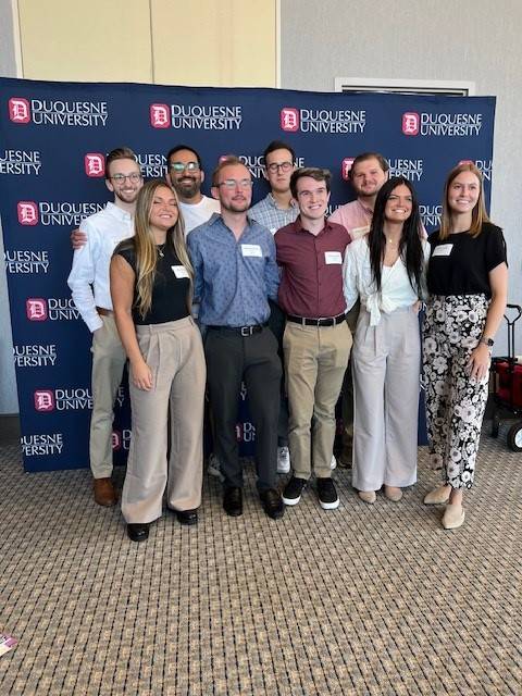 group of Duquesne alumni smiling in front of Duquesne backdrop