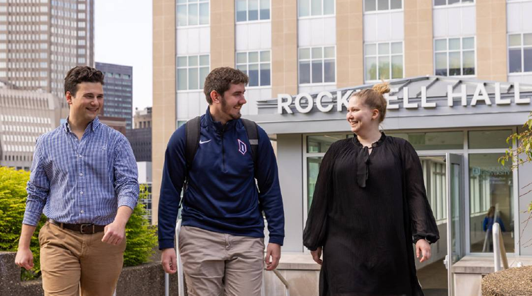 Three smiling students walk out of Rockwell Hall.