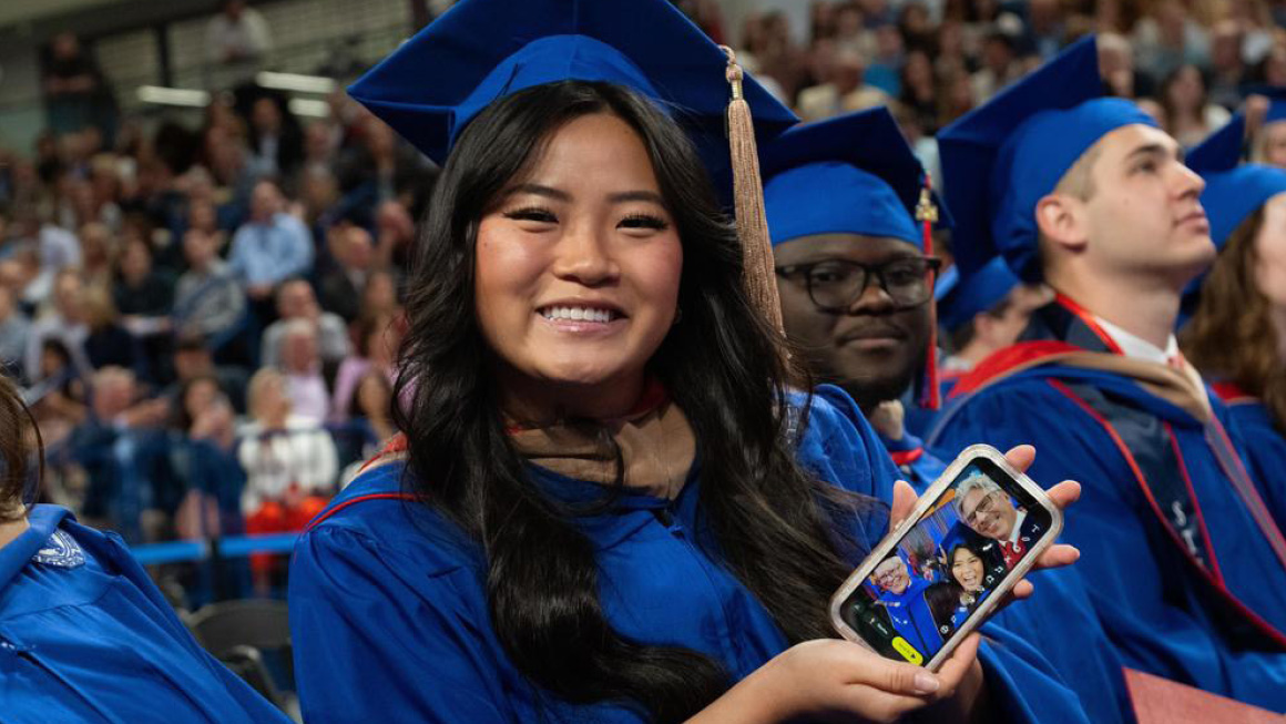 Happy graduate shows her cell phone with a selfie with President Ken Gormley.