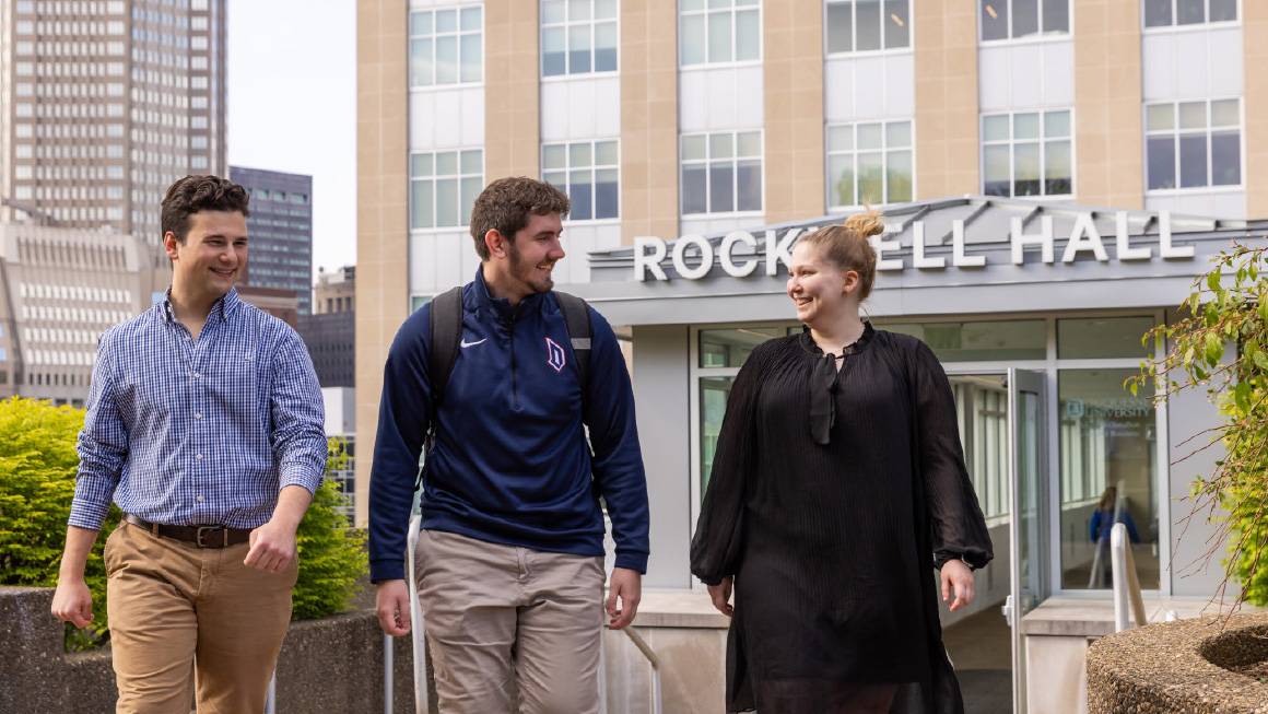 Three smiling students walking out of Rockwell Hall.