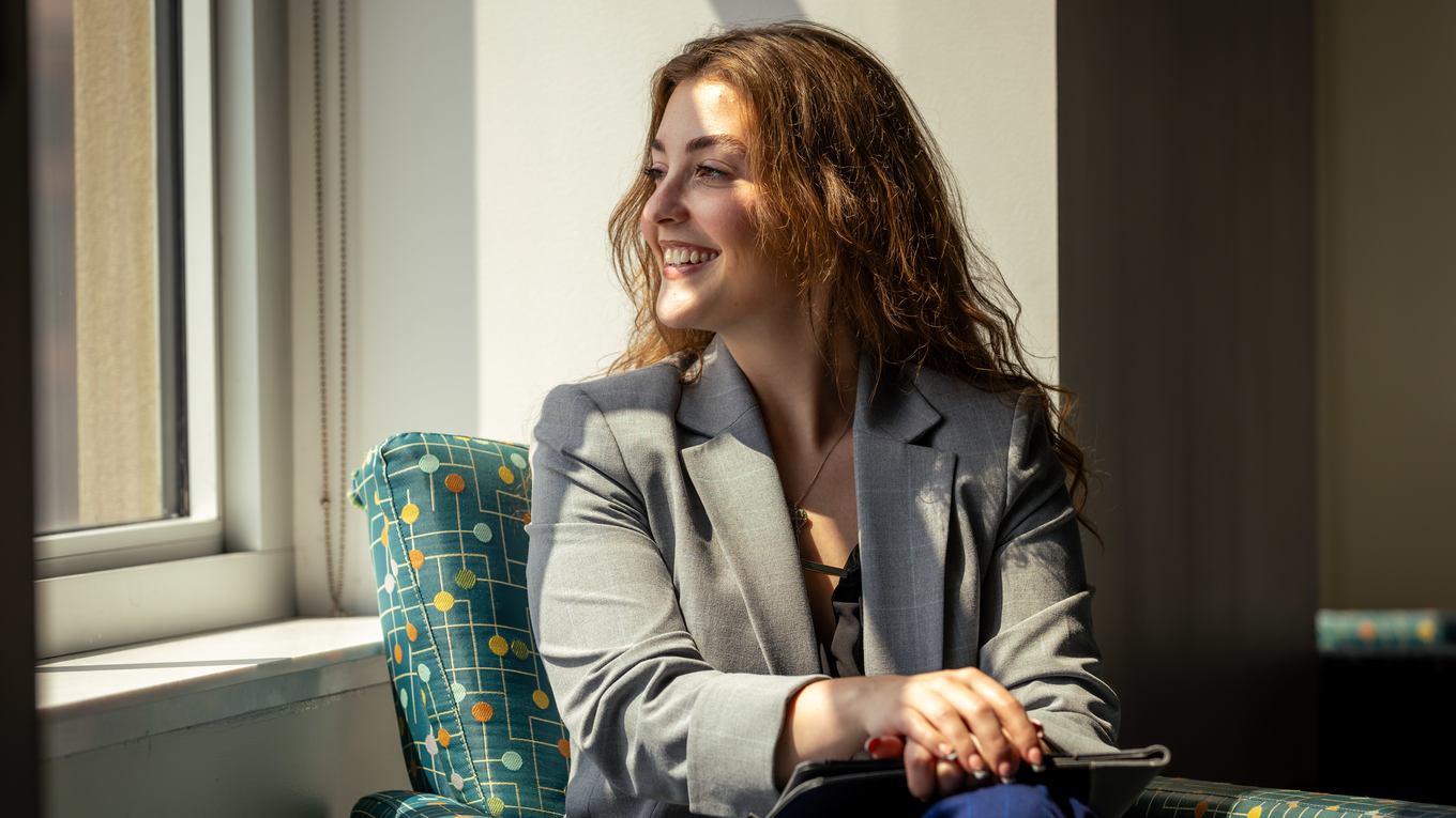 A graduate students looks out of a window and smiles.