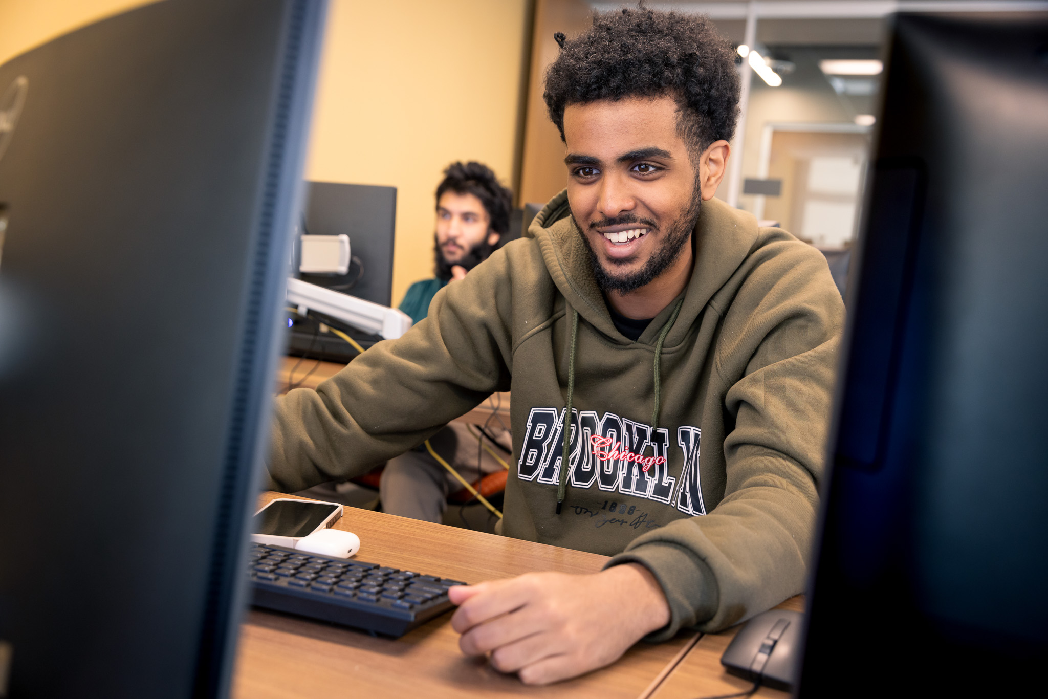 A student smiles while working on a computer in a lab.