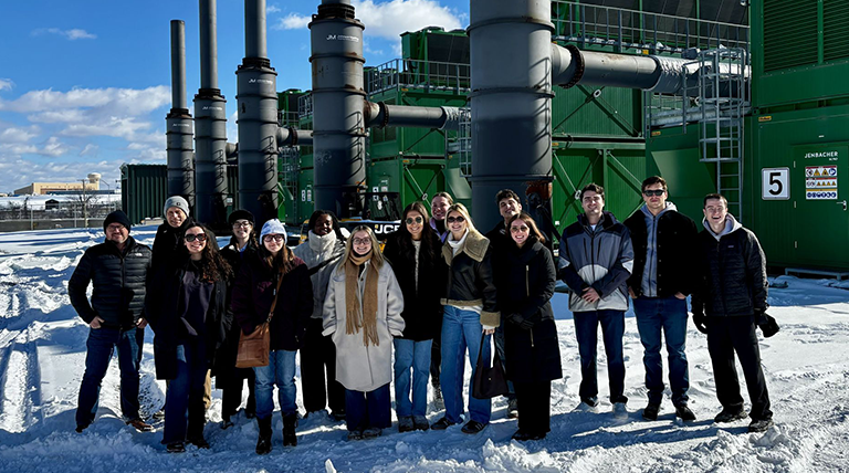 A group of students and a professor pose on site at a power plant. 