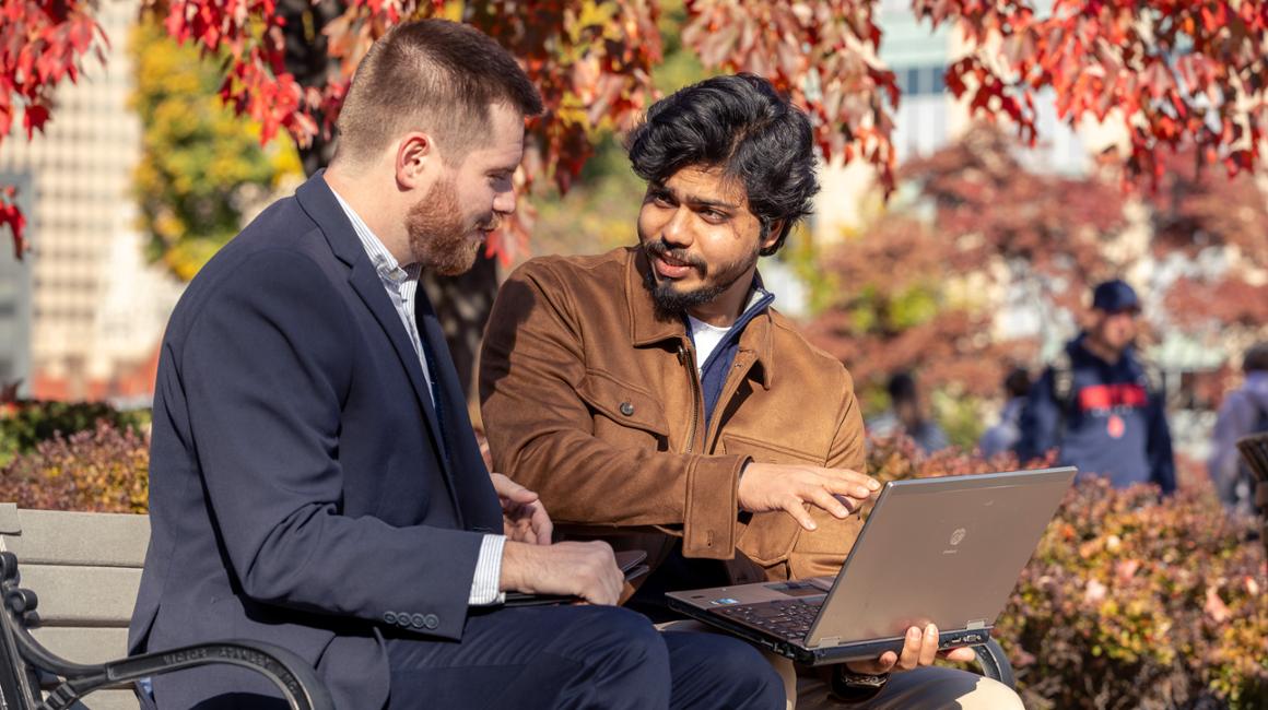 Graduate students look at a laptop outside.