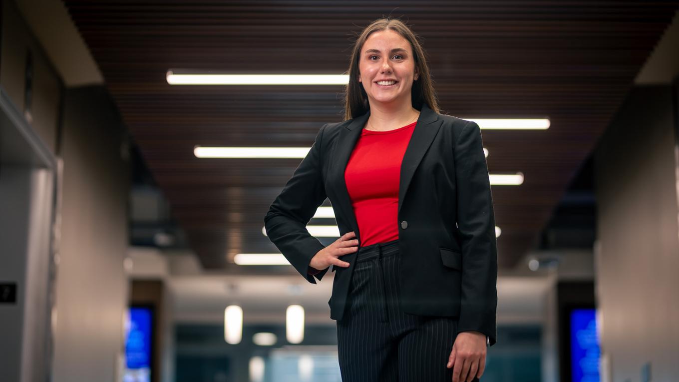 A business student wearing a suit stands with her hand on her hip.