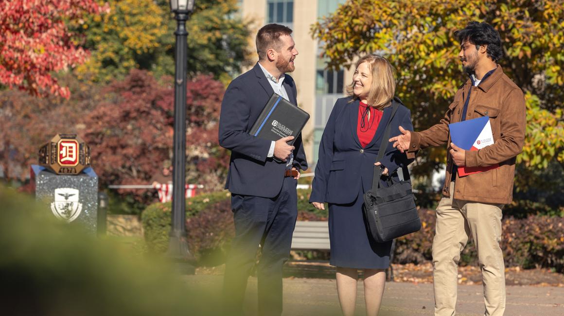 Graduate students talk outside on Duquesne's campus near the ring statue.