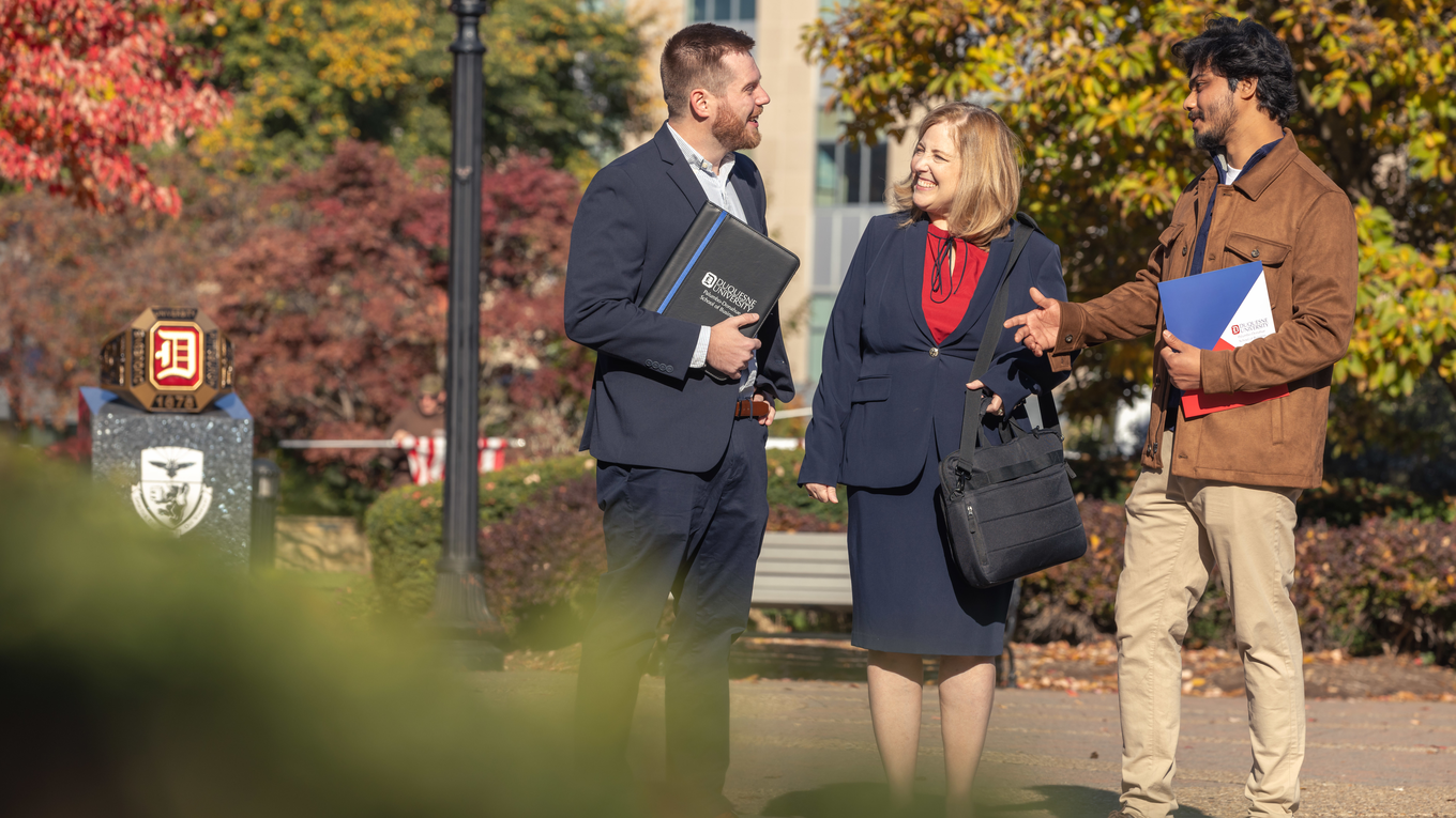 Graduate students talk outside next to the Duquesne University ring statue.