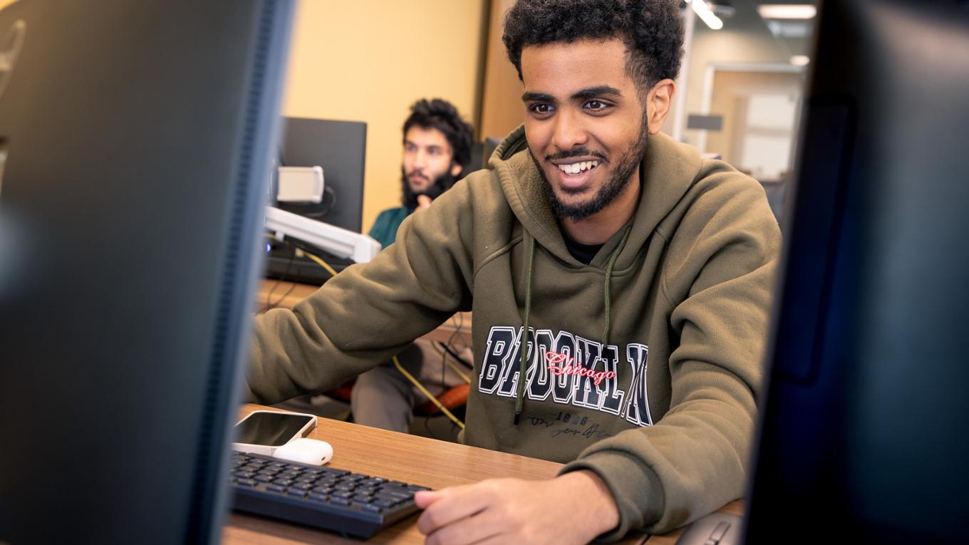 A student smiles while working on a computer in a lab.