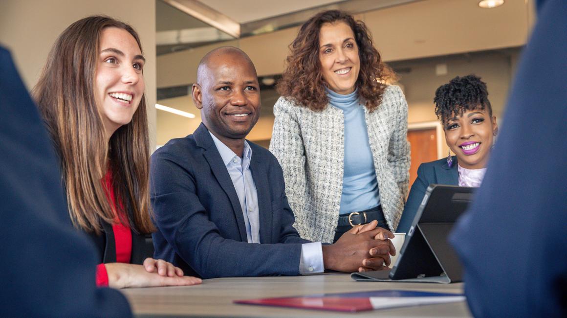 A professor and graduate students smile in a conference room.