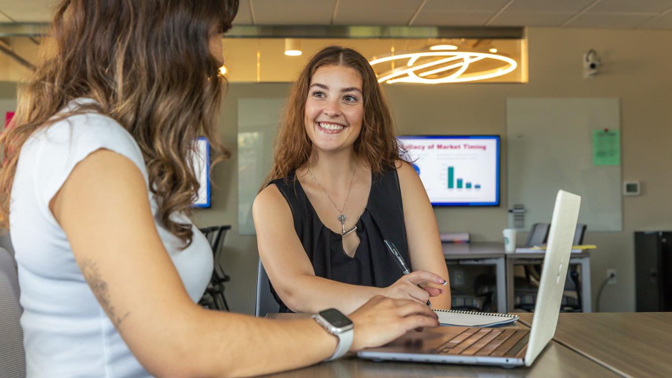 A management student smiles while meeting with a peer.