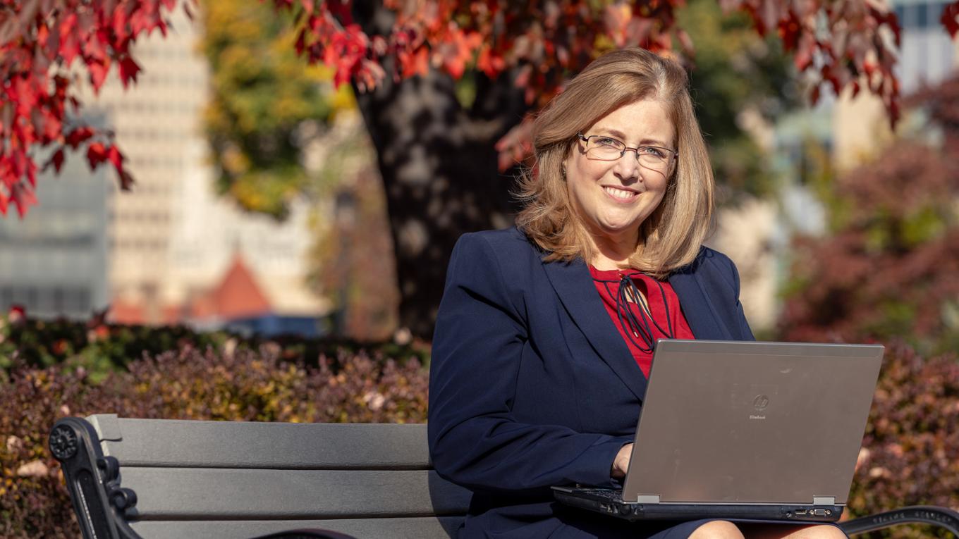 A professional woman works outside on a laptop.