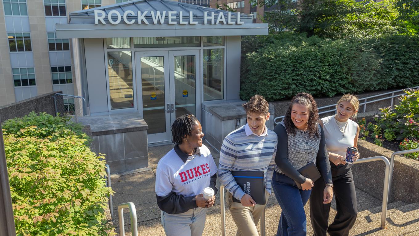 Students walk out of Rockwell Hall's entrance, smiling. 