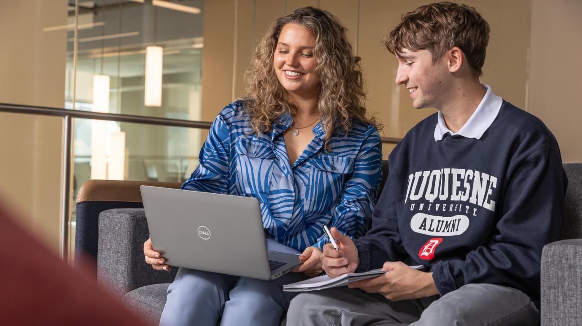 Two MBA students smile while looking at a laptop.