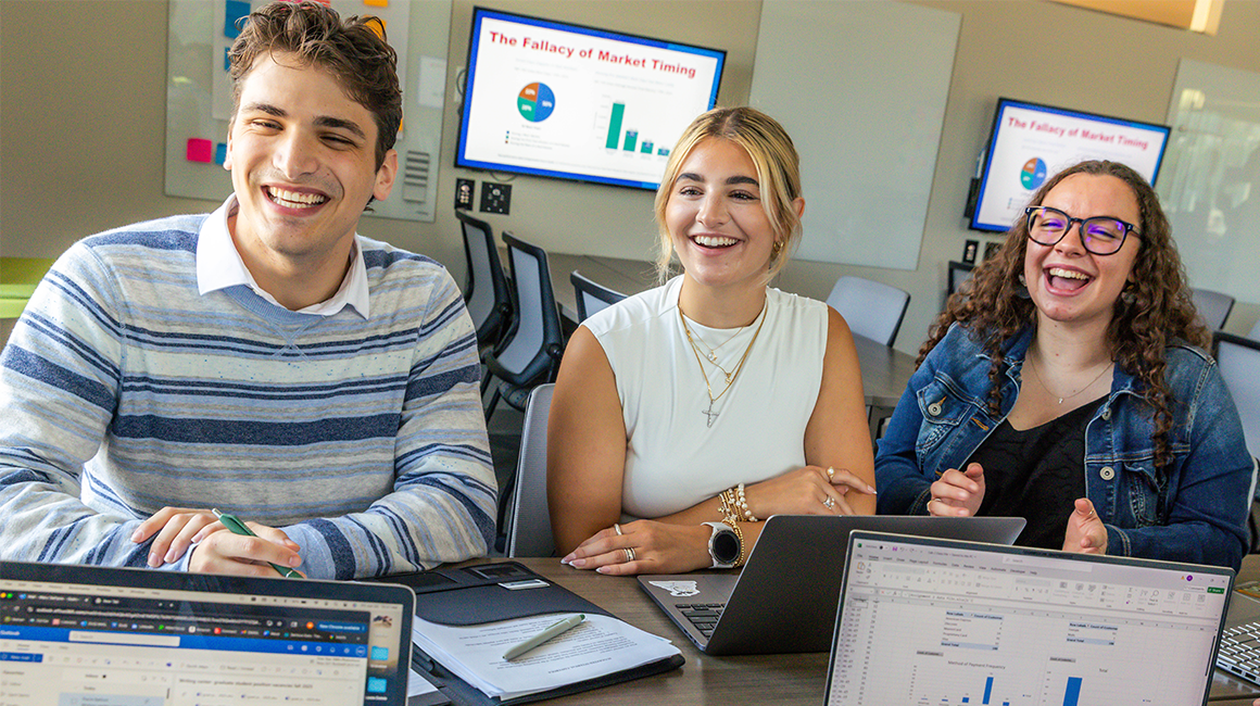 Three MBA students smile and laugh while working on a group project.