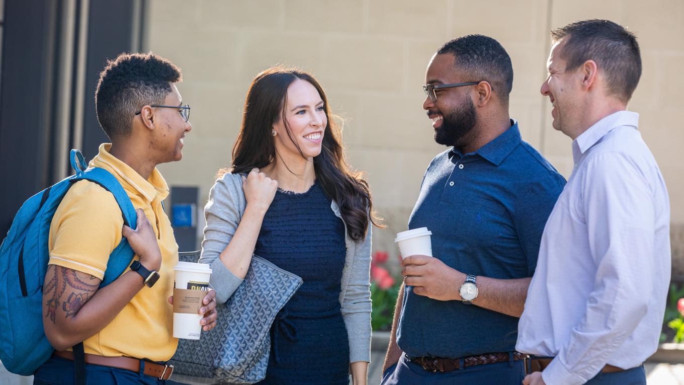 A group of professionals stand outside drinking coffee. 