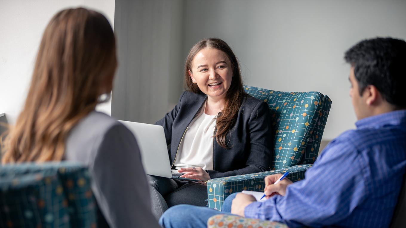 Professionals converse while sitting in patterned chairs.