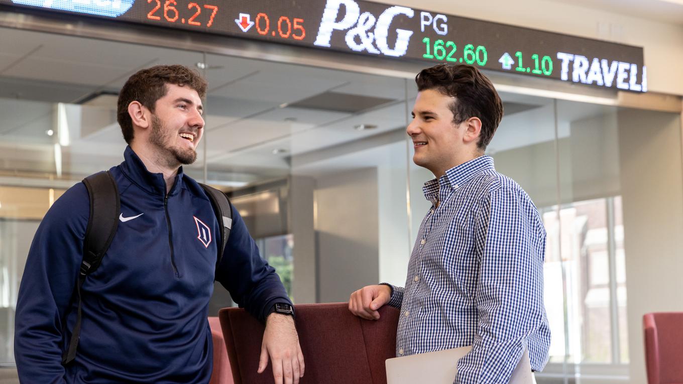 Business students chat in front of a stock ticker.