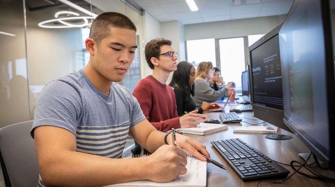 A student takes notes in a computer lab. 