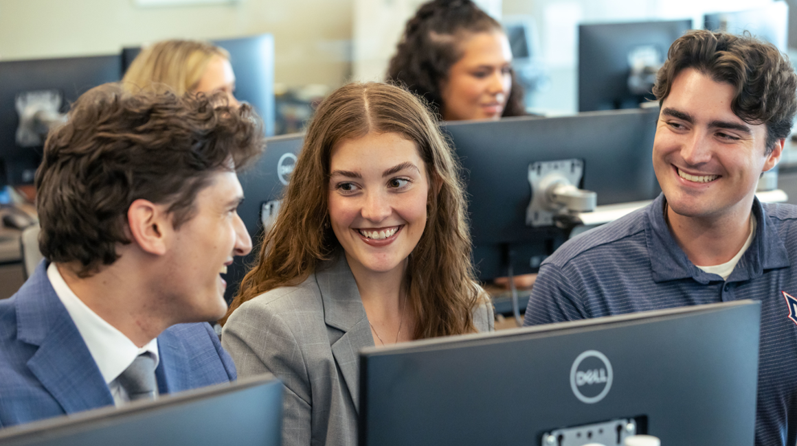 Graduate students smile at one another in a computer lab.