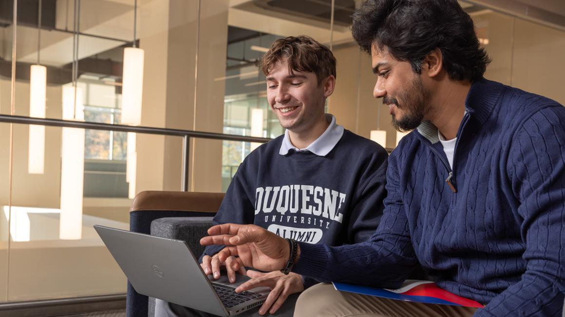 Two students collaborate on a laptop.