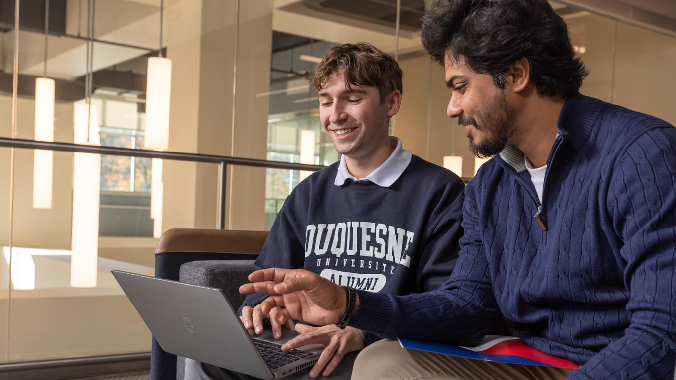 Two students collaborate on a laptop.