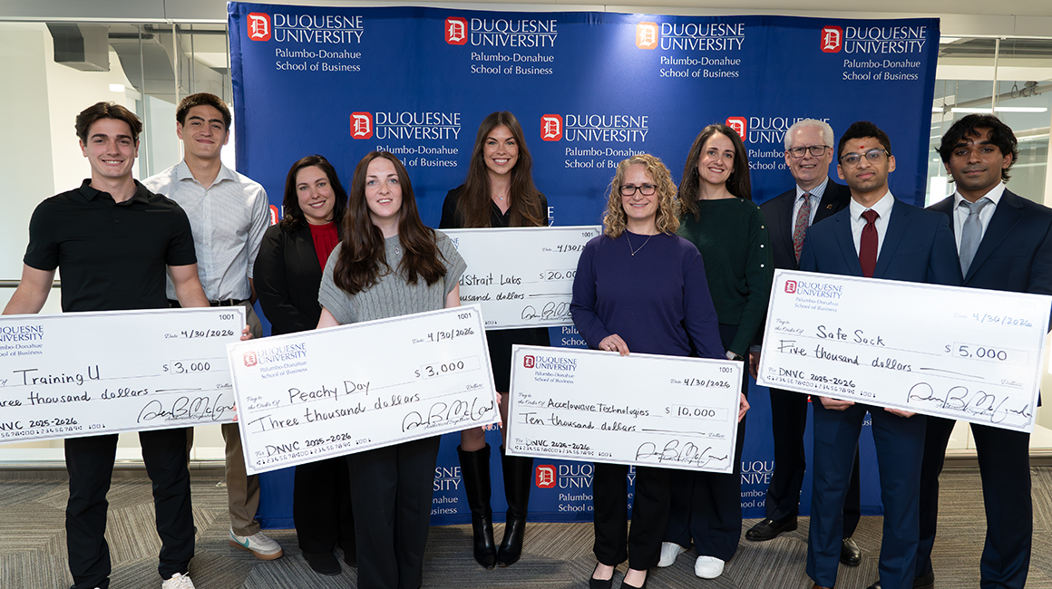 The winners of the Duquesne New Venture Challenge holding their checks in front of a School of Business backdrop.
