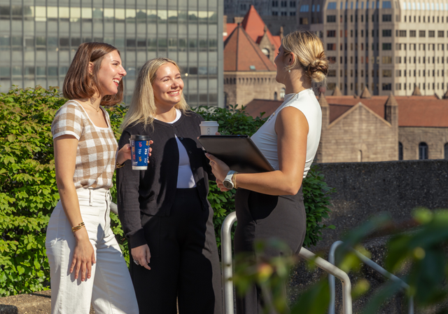 Three business professionals standing on Duquesne's campus, overlooking downtown Pittsburgh
