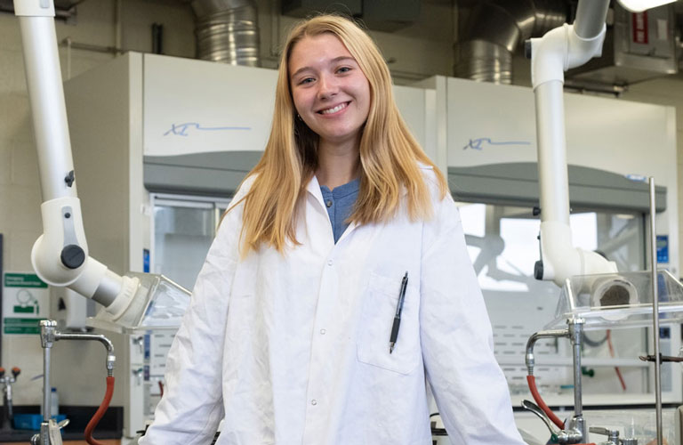 Madeline Sclichter standing in lab, wearing white lab coat