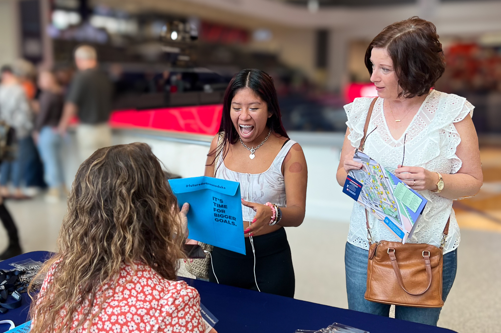 Admitted student smiling big next to parent as staff hands her accepted student packet at Duq Day in auditorium