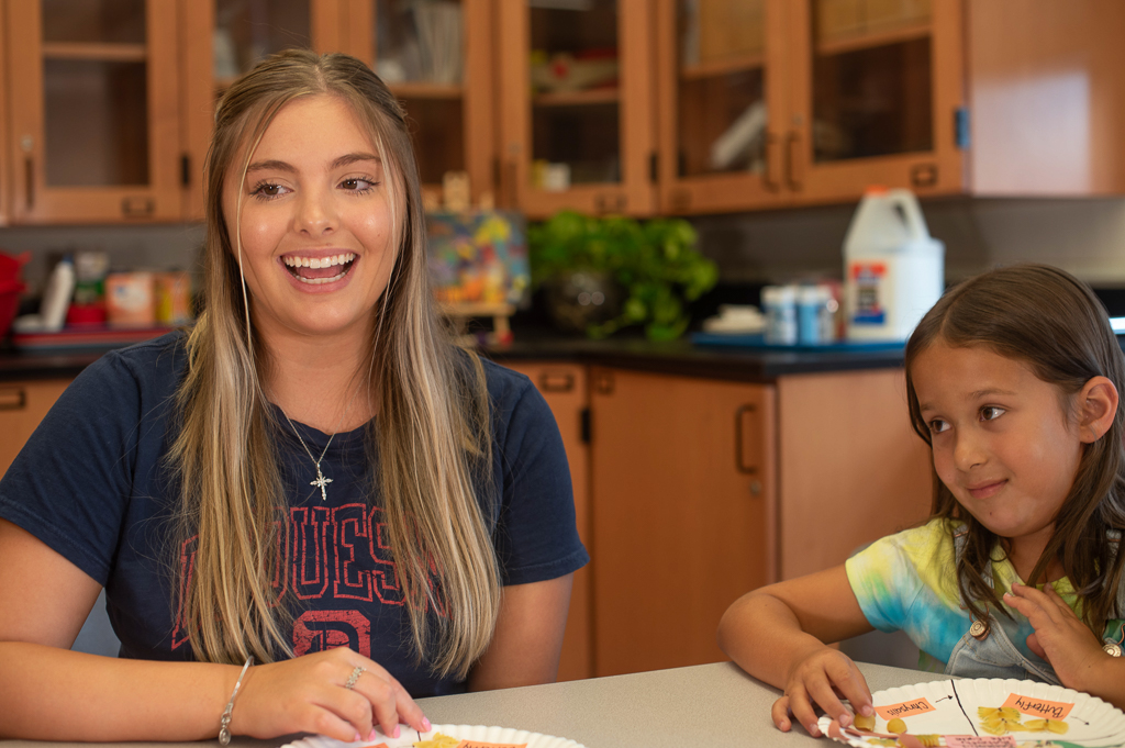 Duquesne student teacher engaging in lesson at table with K-12 student next to her in clasroom with paper plate science project