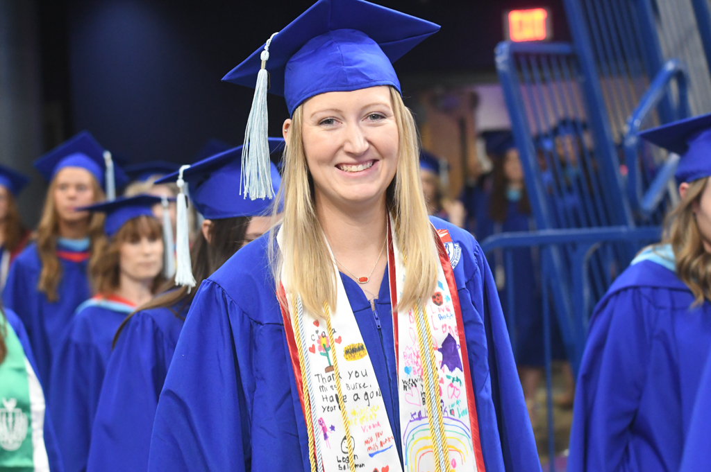 School of Education scholarship student graduating smiling at viewer while in graduation regalia on commencement floor. 