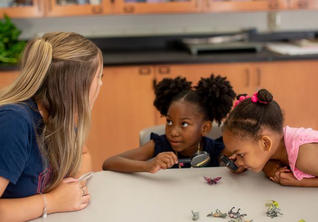 Student teacher with prek students engaging in scienc eactivity with magnifying glass and plastic animal figurines