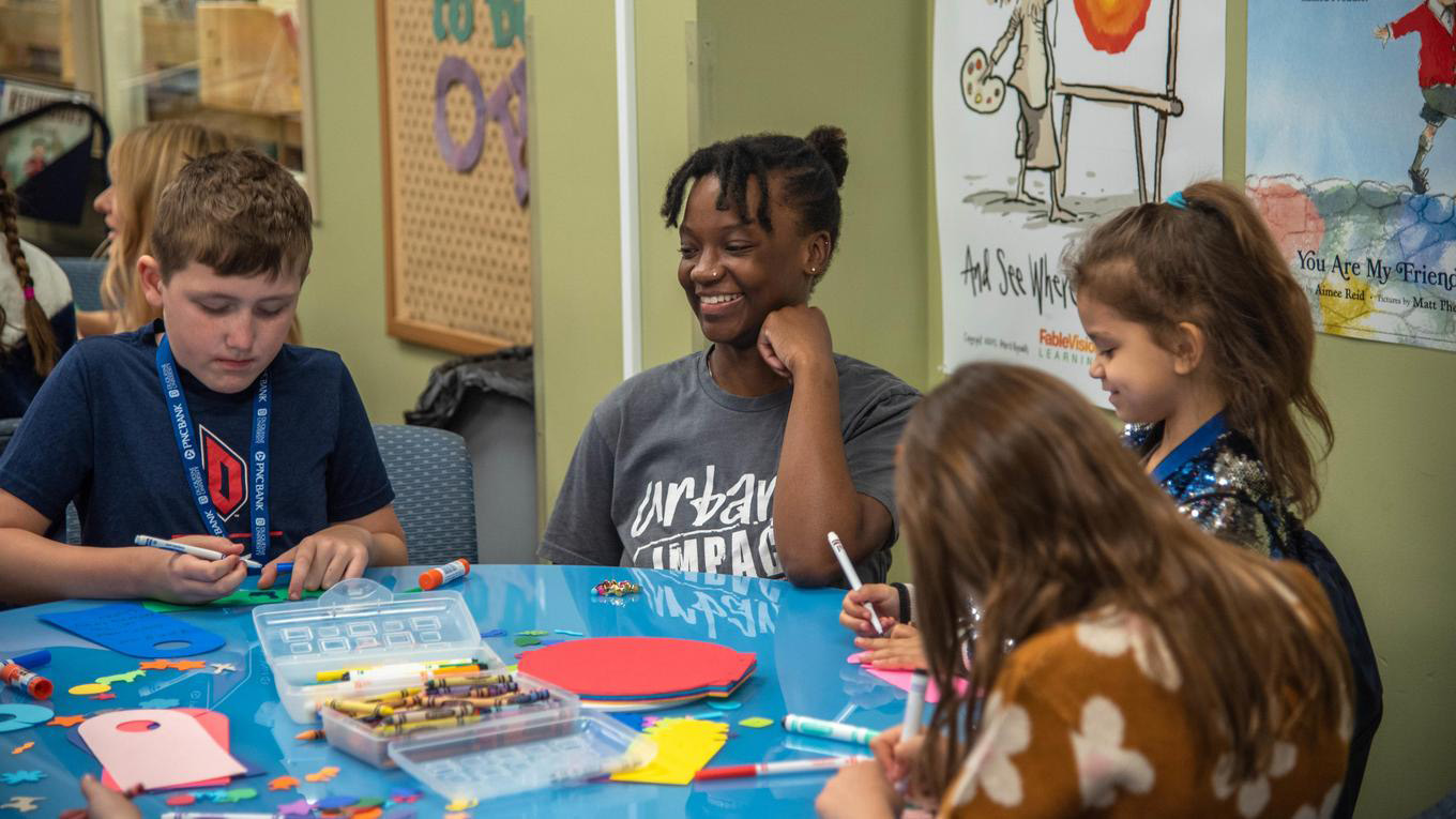 Duquesne School of Education undergraduate student works at a table with children in the Curriculum Center on campus.