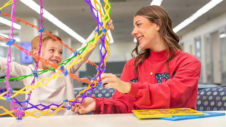 Duquesne School of Education student works with small child using expandable toy ball.