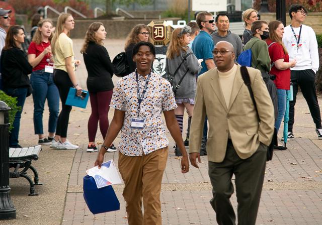 Father and son walking on campus during DUQ Days admission event outside on campus by Duquesne ring and fall leaves and campus activity in the background