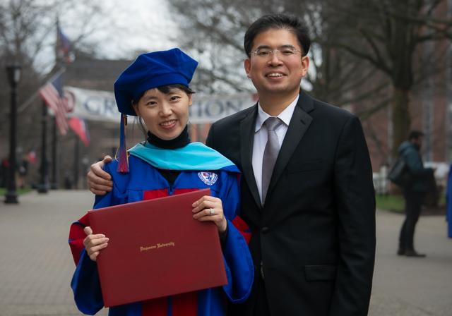 School of Education graduate holding diploma next to spouse, with both smiling outside on Academic Walk on Winter Commencement