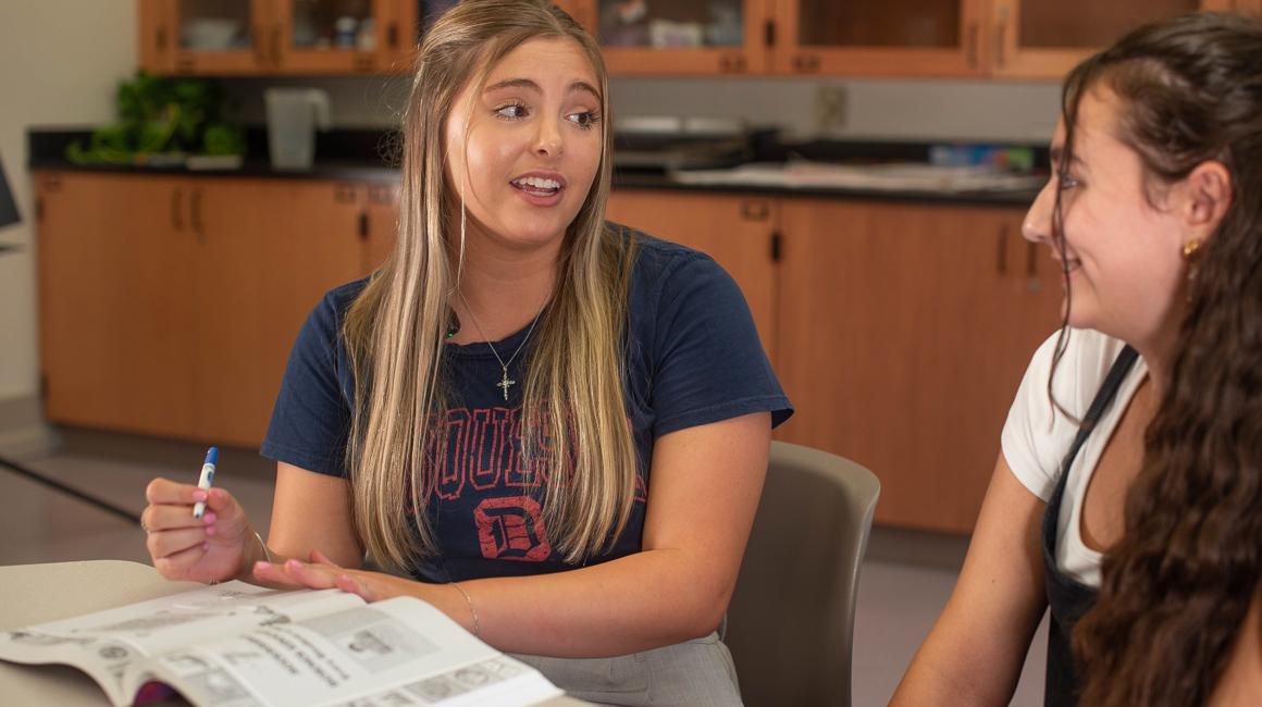 Duquesne middle level education student teacher discussing lesson with book with Grades 4-8 student in the field in a classroom