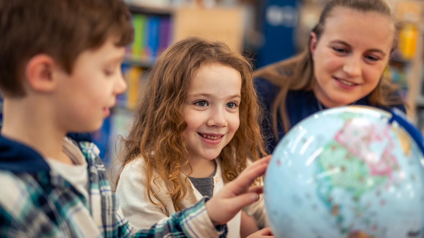 Elementary school teacher with school children in classroom engaging in lesson with globe.