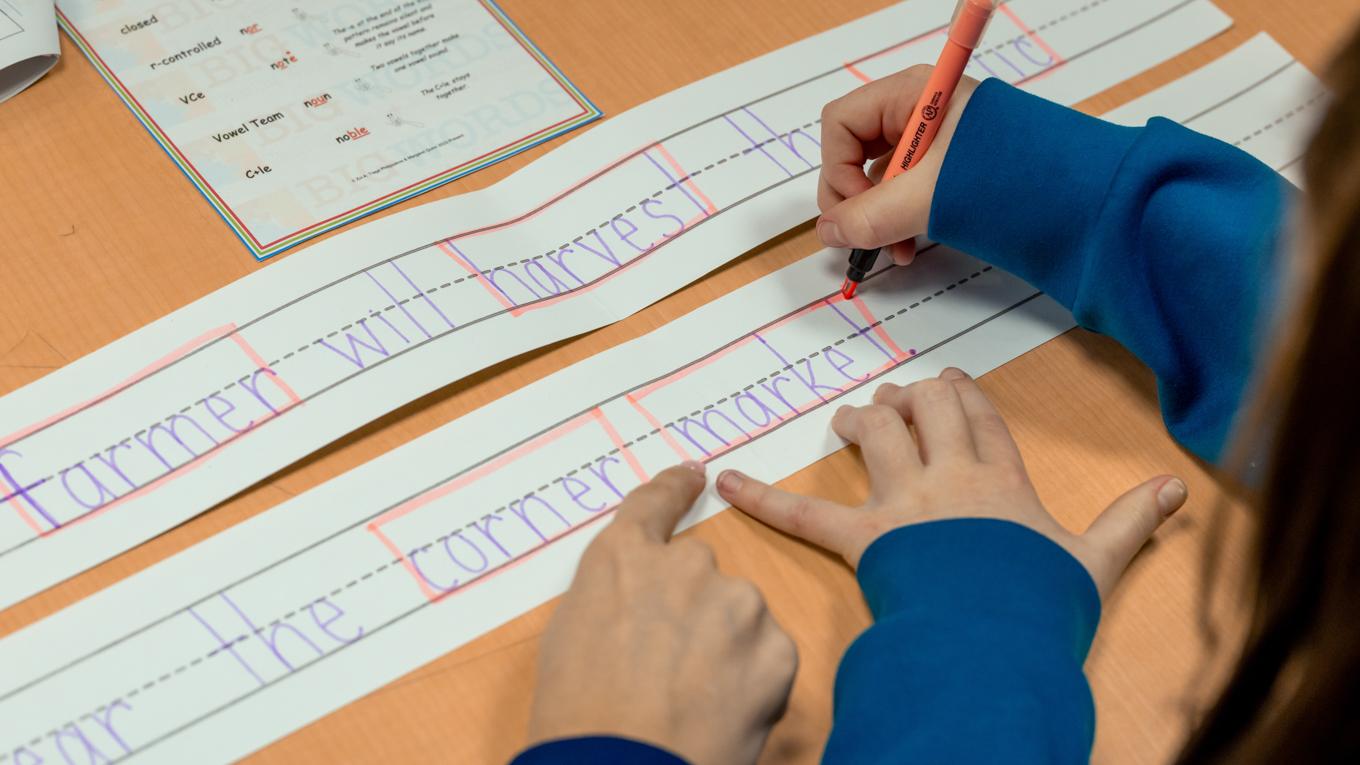 Reading specialist certification for PDE alumni specialist and student hands pointing and highlighting to scentence on dotted line paper
