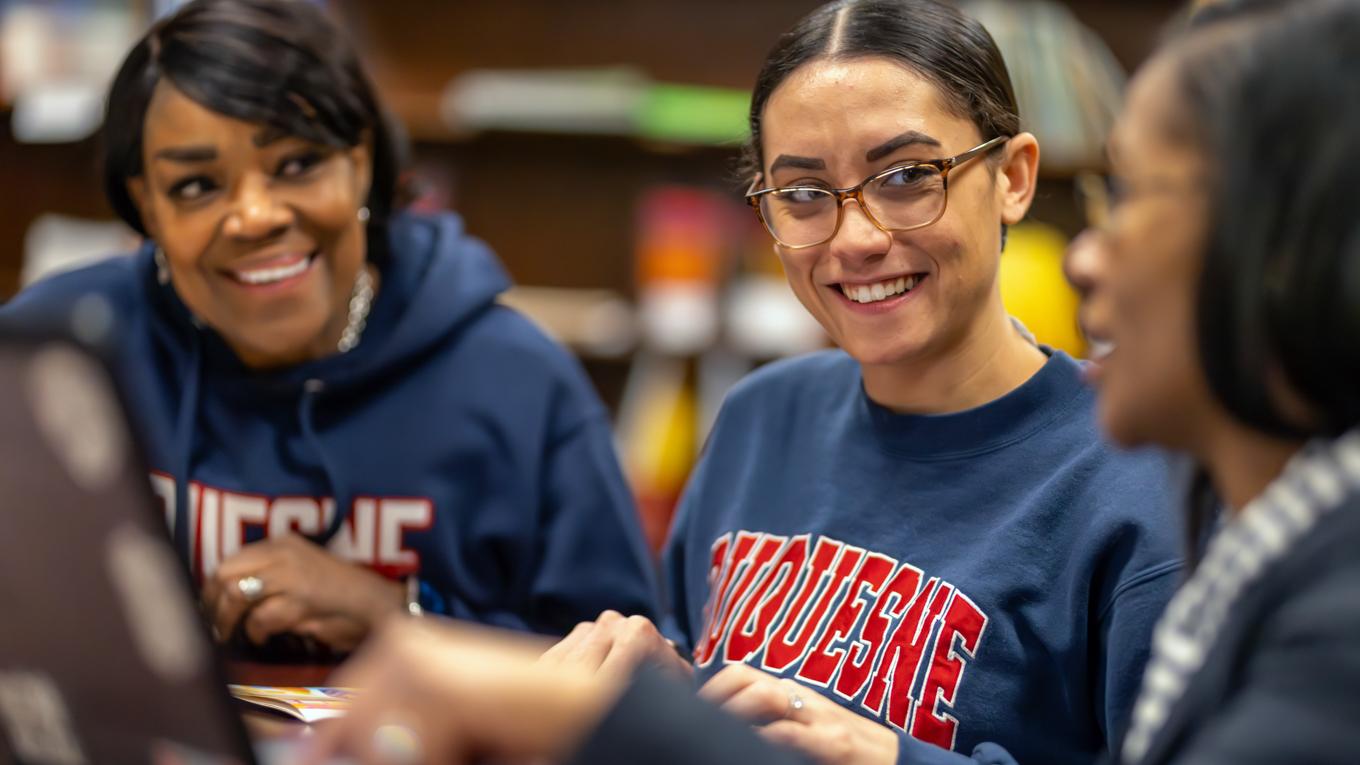 Duquesne Graduate School of Education student in center with laptop with other students on side collaborating on studies.