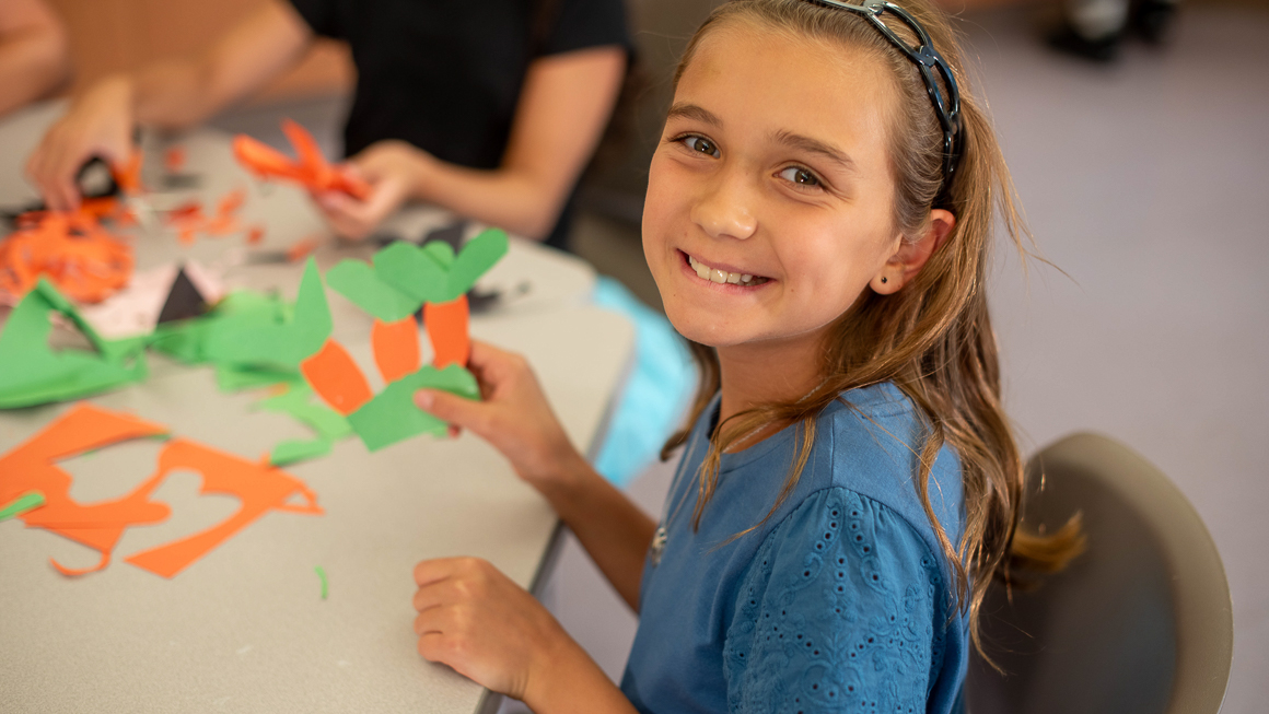 Ten-year-old Molly looking at viewer smiling with construction paper project in front of her at table