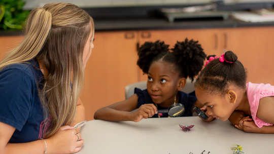 Student teacher with prek students engaging in science activity with magnifying glass and plastic animal figurine