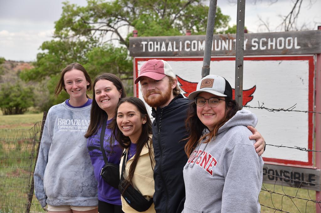 Photo of five School of Education students in New Mexico smiling in group outside with Tohaali Community School sign behind them