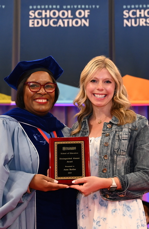 Anne Beitler with alumni award in hand smiling on stage next to School of Education Dean Generett.