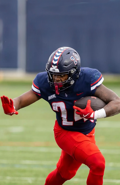 Duquesne B.S.Ed. Middle Level student and Dukes football player Shawn Solomon with football on football field running in his #24 uniform