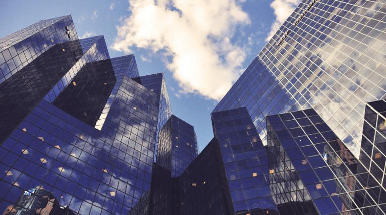 Tops of skyscrapers reflecting the clouds and blue sky.