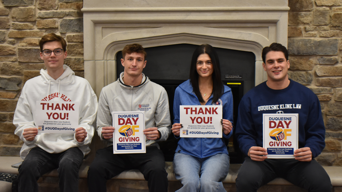 A group of students sitting in front of a fireplace holding "thank you" signs.