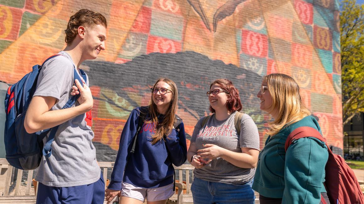 Four Liberal Arts students standing in front of a mural outside Laval House.